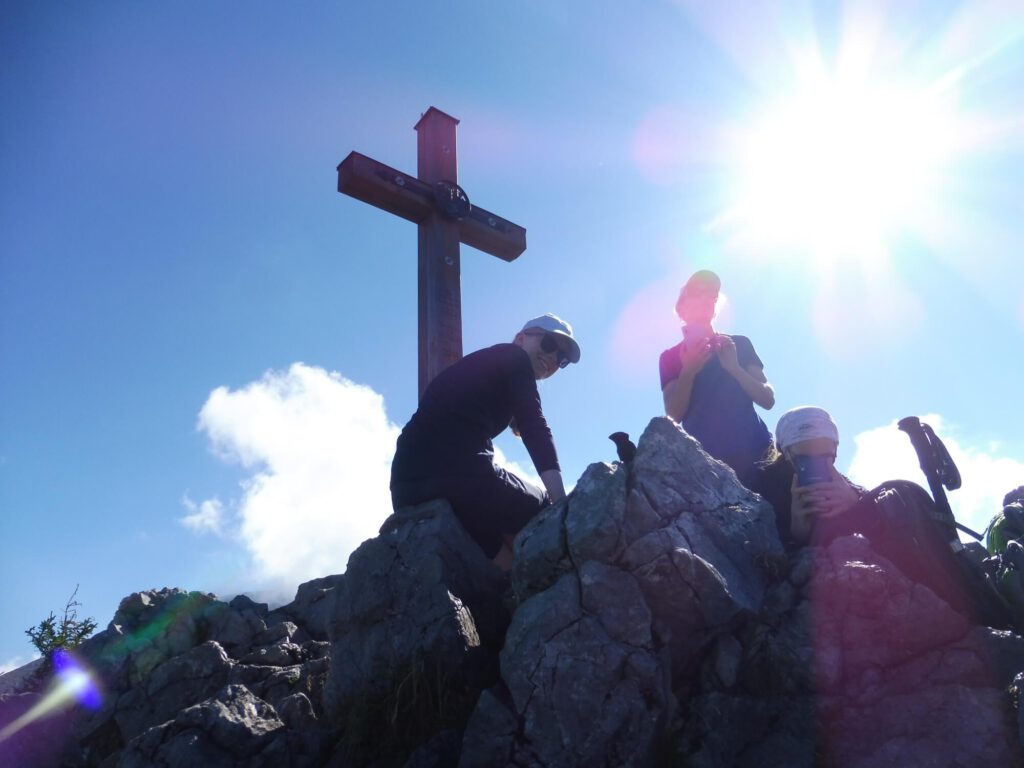 Foto von Wanderern vor einem Gipfelkreuz im Gegenlicht.