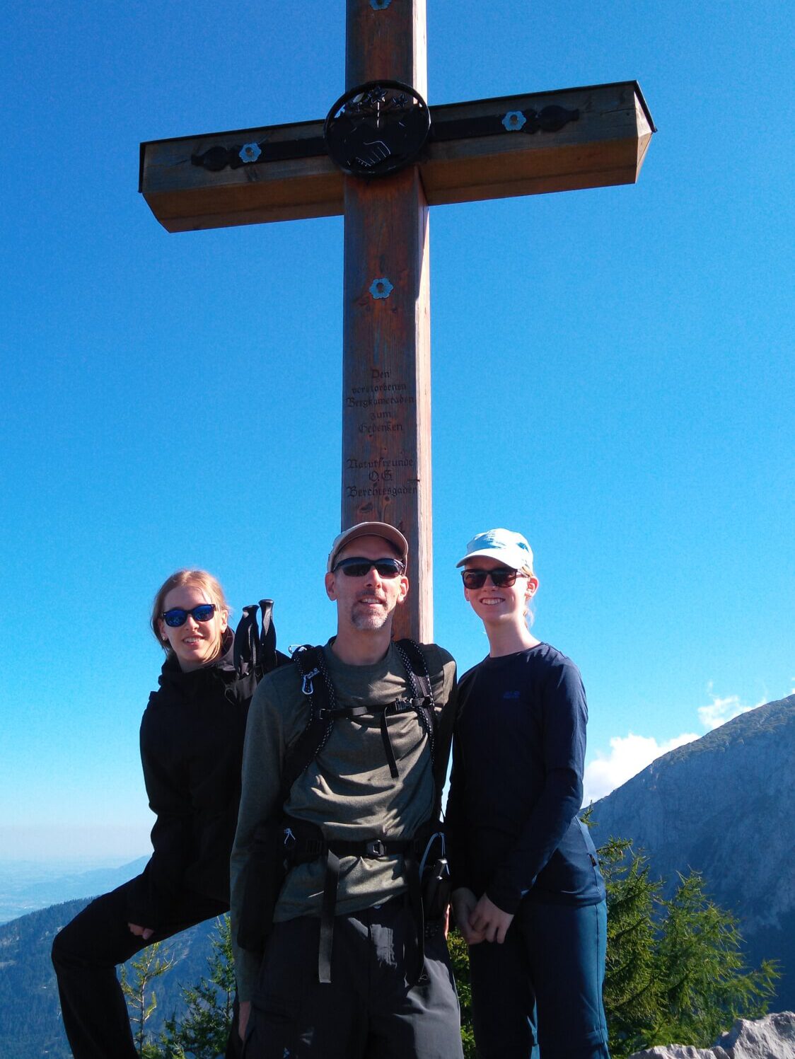 Foto von Personen vor einem Gipfelkreuz vor dem strahlend blauen Himmel.