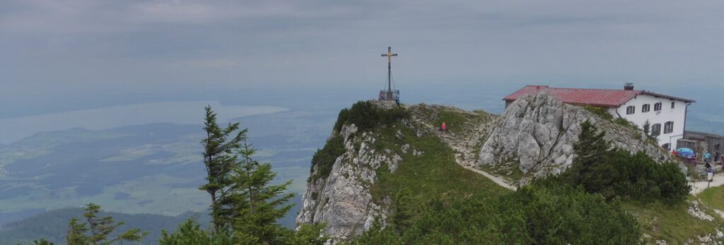 Foto eines Gipfelkreuzes in kurzer Entfernung vor einem Bergabhang. Im Hintergrund eine Schlechtewetterfront.