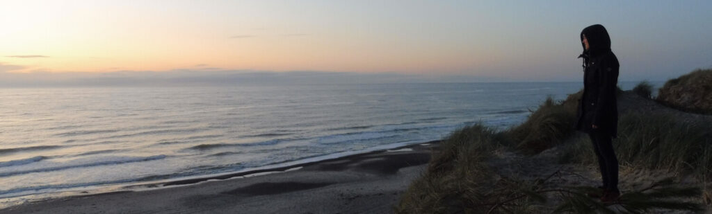 Eine einzelne Person blickt zufrieden im Sonnenuntergang auf das Meer hinaus. Ausdruck von MEERwert.