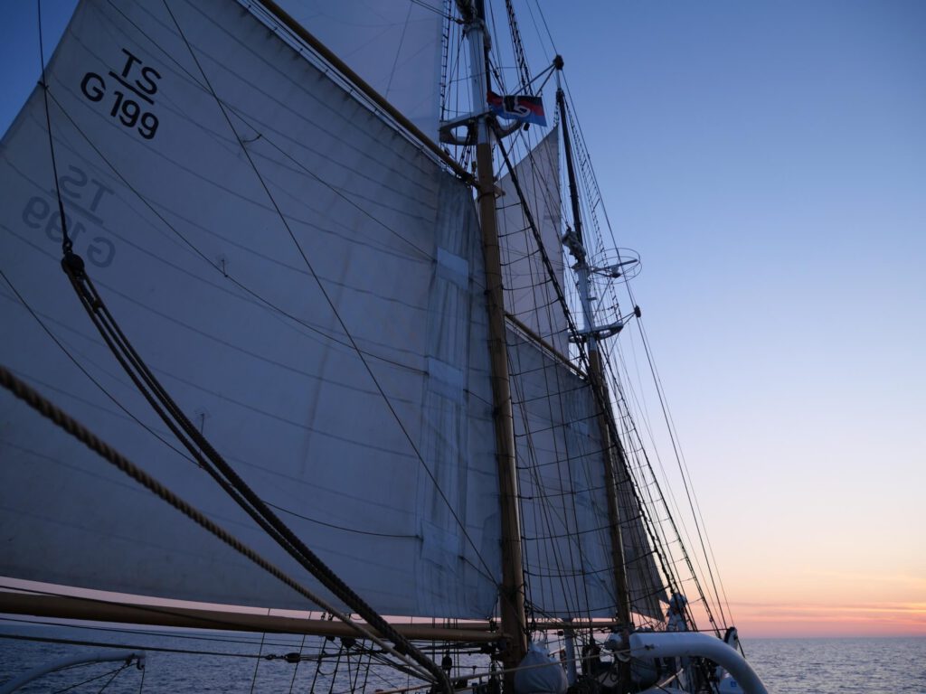 Vater-Tochter-Glücksmomente: Auf der Nordsee an Bord der Großherzogin Elisabeth. Blick auf das Rigg des in den Wind gestellten Schoners und des Großsegels. Im Hintergrund der Sonnenaufgang.