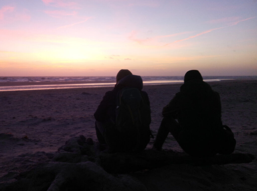 Foto von Volker Schwolow: Zwei Männer sitzen am Meer beim Sonnenuntergang und blicken auf das Meer hinaus.
