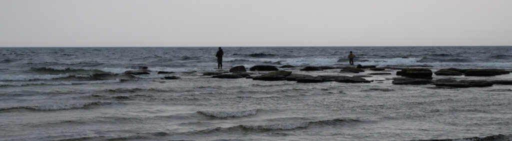 Mein Kraftort das Meer: Männer stehen auf Stehsteinen im Meer und angeln.