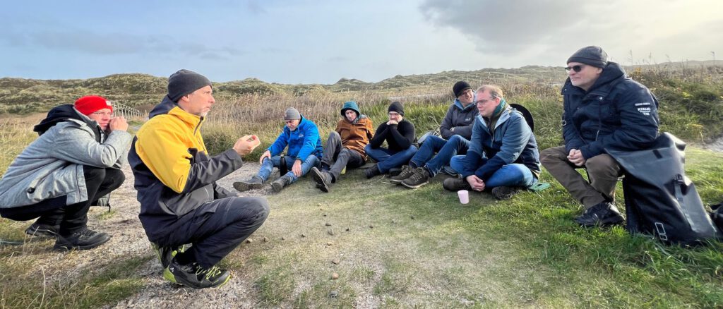 Naturcoach Volker Schwolow erläutert einer Gruppe von Männern das Rad der Jagd während einer Männerauszeit am Meer.