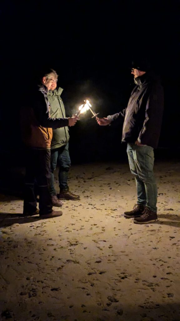 Männer mit Fackeln am Strand in der Dunkelheit.