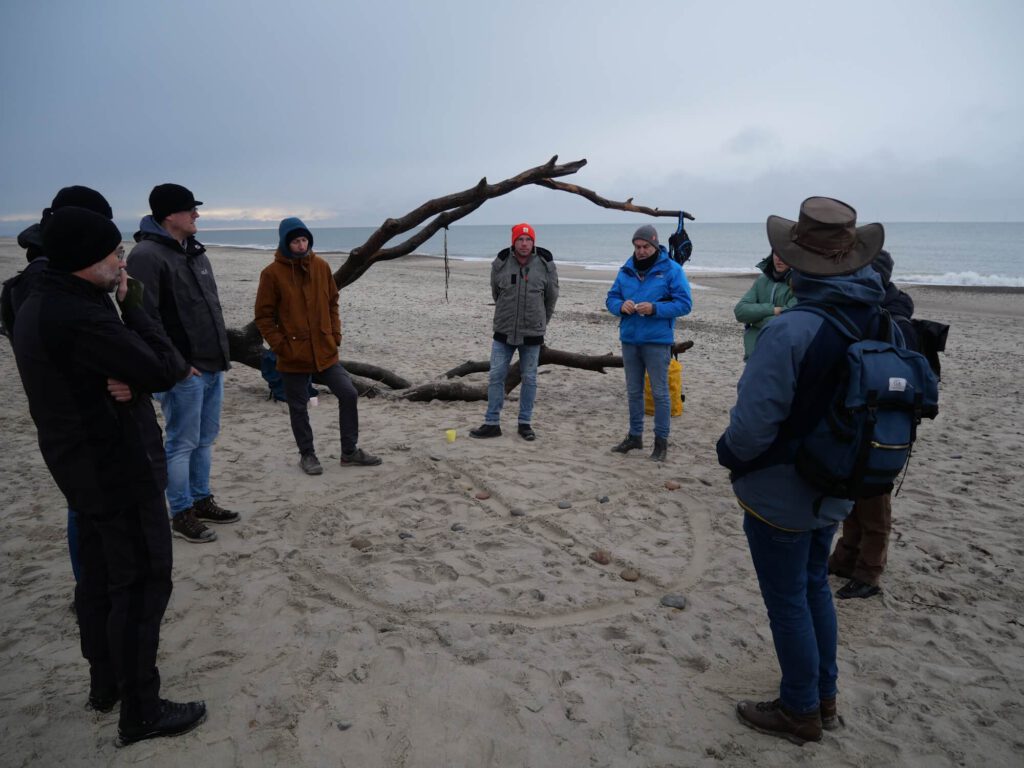 Männerkreis um das Rad der Jagd am Strand.